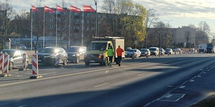 Ceļa remontdarbi Lielajā ielā pie Hercoga Jēkaba laukuma – satiksme vienā joslā, automašīnu rinda un divi ceļstrādnieki pie darba furgona.