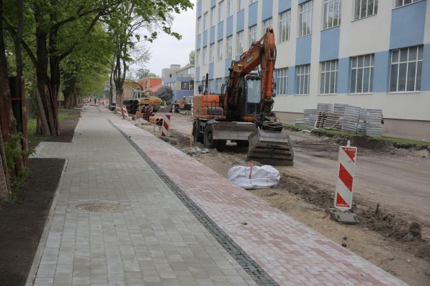 Brieza_iela Ielas pārbūve pie ēkas. Ekskavators un strādnieki veic darbus, uzstāda norobežojumus. Ietve no dažādu krāsu bruģa.