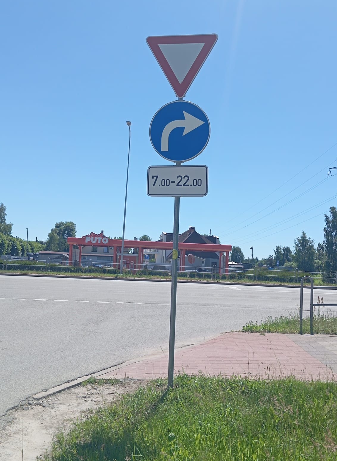 Ceļa zīme ar priekšrocības došanas zīmi un norādi pagriezties pa labi, kas spēkā no plkst. 7.00 līdz 22.00 1.līnijas krustojumā ar Dobeles šoseju. Fonā redzama degvielas uzpildes stacija.