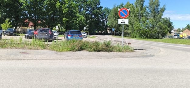 Salnas iela Ceļa zīme “Apstāties aizliegts” ar papildzīmi, kas norāda aizlieguma sākumu pēc 15 metriem pa kreisi. Fonā redzama autostāvvieta, koki un ceļš.