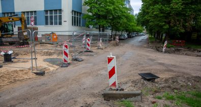 barona-kalpaka-krustojusms-remonta-scaled Ielas krustojuma remontdarbi pilsētvidē ar norobežojošām metāla sētām, vadstatņiem un ekskavatoru fona.