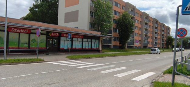 Kalpaka-iela_small Pulkveža Oskara Kalpaka iela ar gājēju pāreju, daudzdzīvokļu dzīvojamo ēku. Gar ielu novietotas ceļa zīmes, fonā koki un mākoņainas debesis.