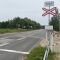 Prohorova iela pie dzelzceļa pārbrauktuves. Redzamas brīdinājuma zīmes, 30 km/h ātruma ierobežojums, pārbrauktuves barjeras, ceļmala ar zāli un ēkas.