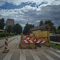 Cel̦a remontdarbi pilsētā ar barjerām, dzeltenām sienām un brīdinājuma gaismām. Tālumā redzamas mājas un mākoņainas debesis.