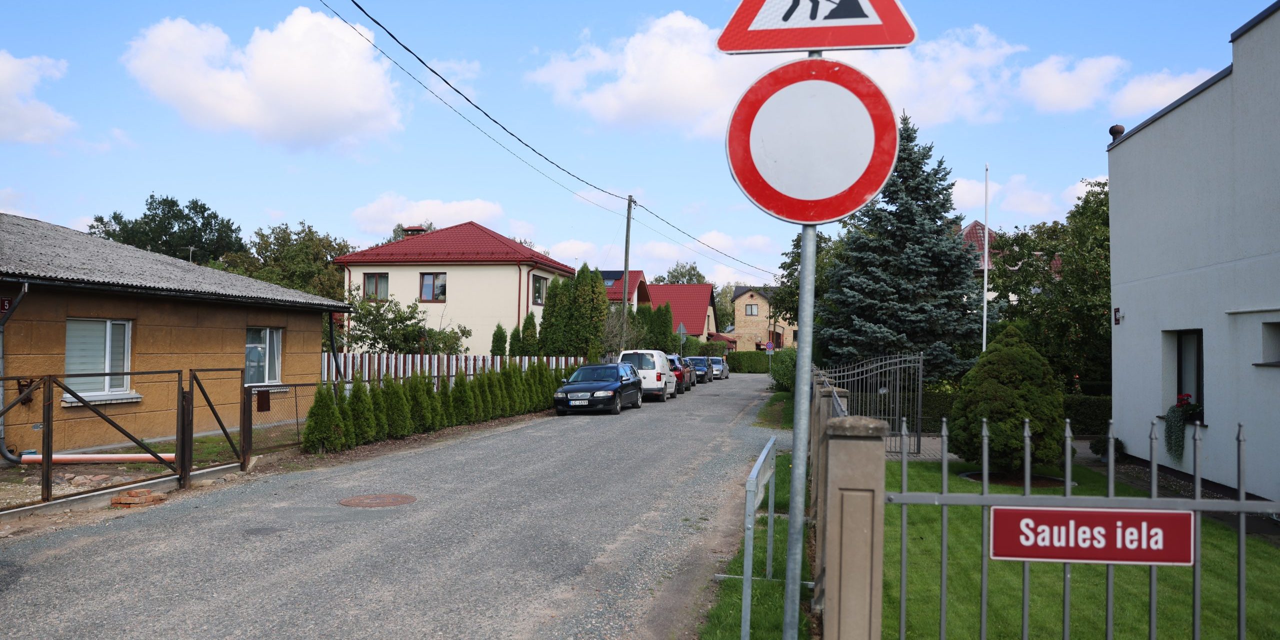 Saules iela ar grants segumu un māju rindām; priekšplānā ceļa zīmes „Ceļa darbi” un „Braukt aizliegts”.