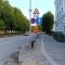 Pilsētas ielas skats ar ietvi un ceļa zīmju stabu, uz kura redzams dzeltenais ātruma ierobežojums 40 km/h, gājēju pārejas brīdinājums un citas ceļa zīmes.