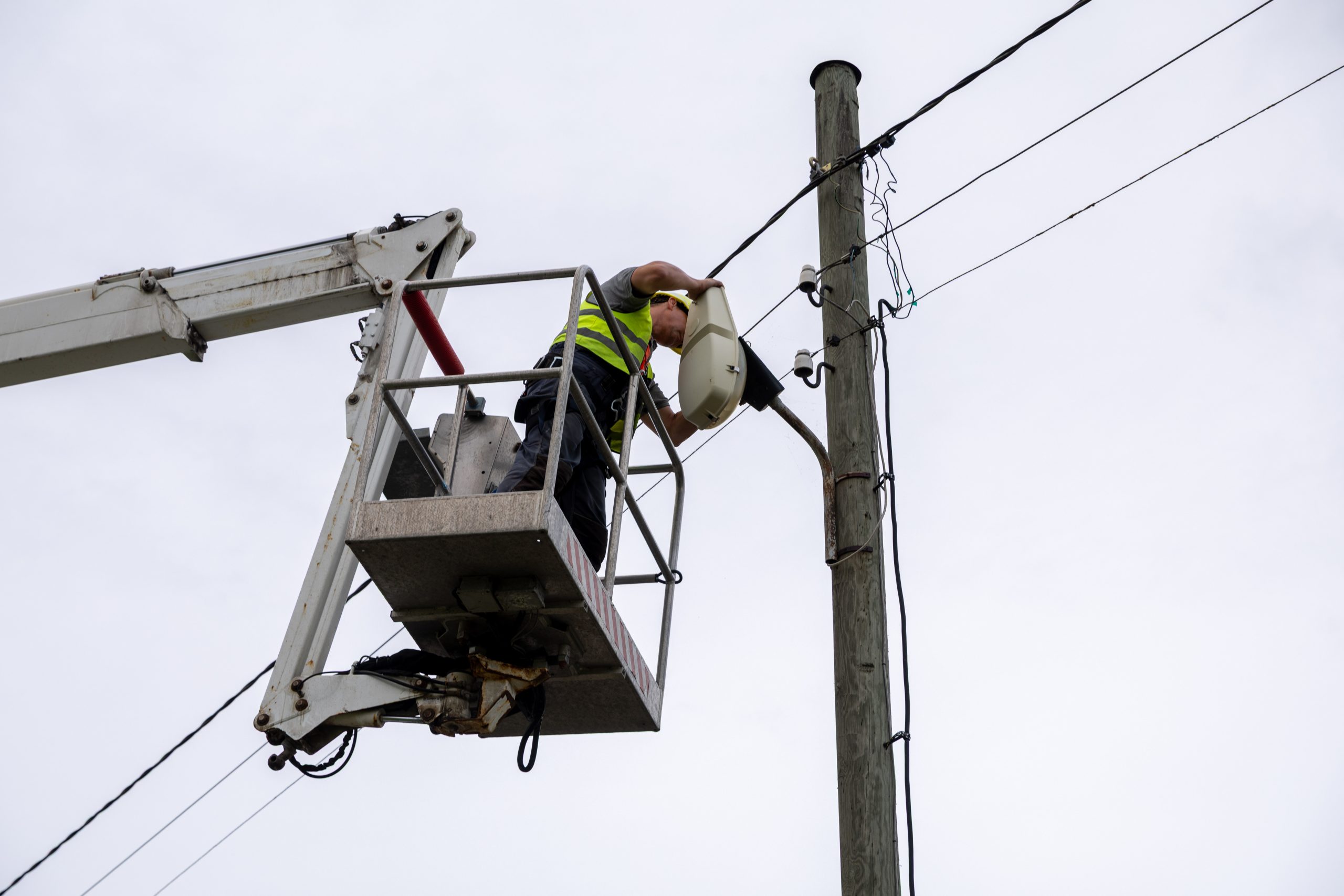 Elektriķis pacēlāja grozā uzstāda jaunu ielas apgaismojuma lampu pie koka staba.